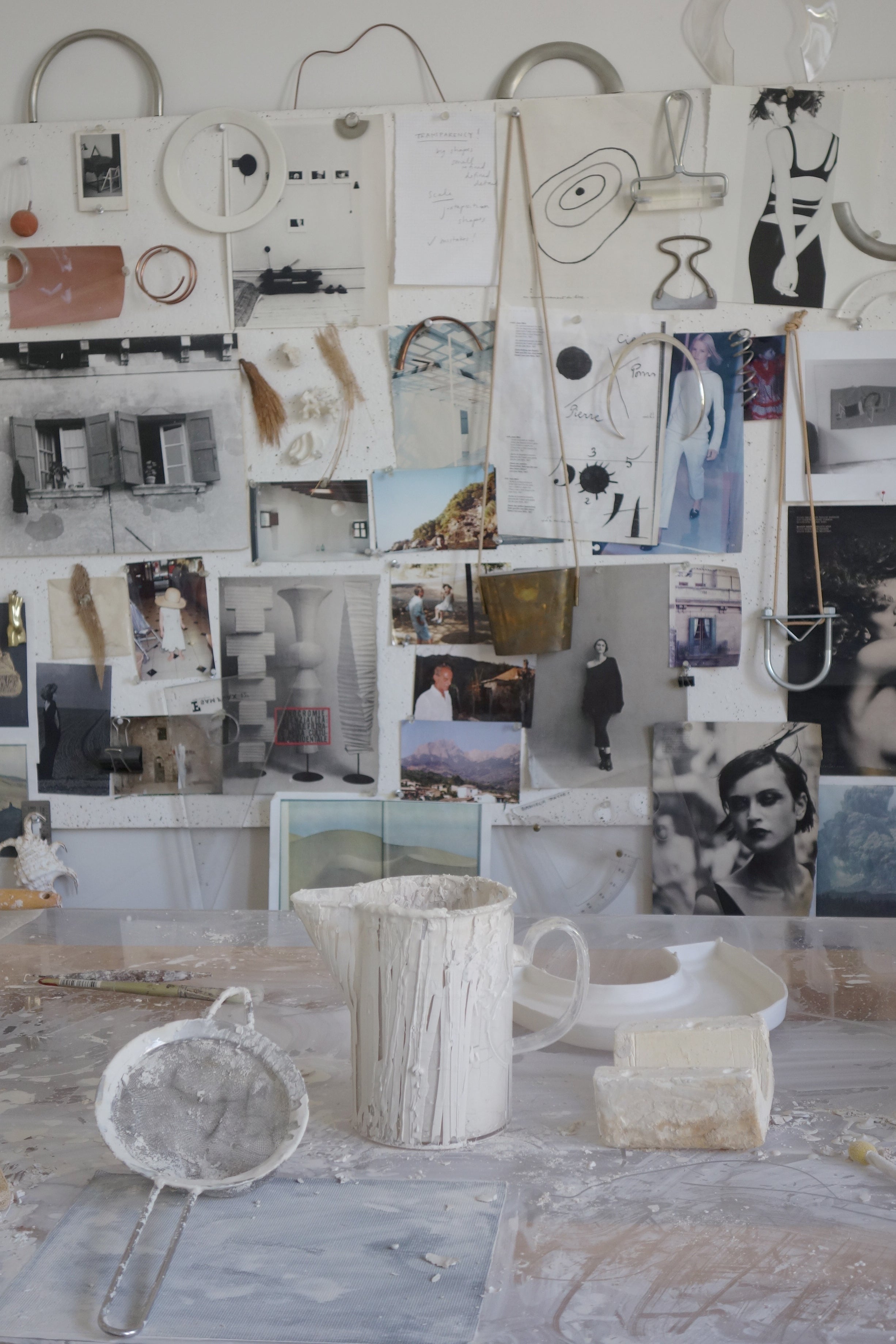 Artistic workspace with various artworks, a mug, and tools on a table.