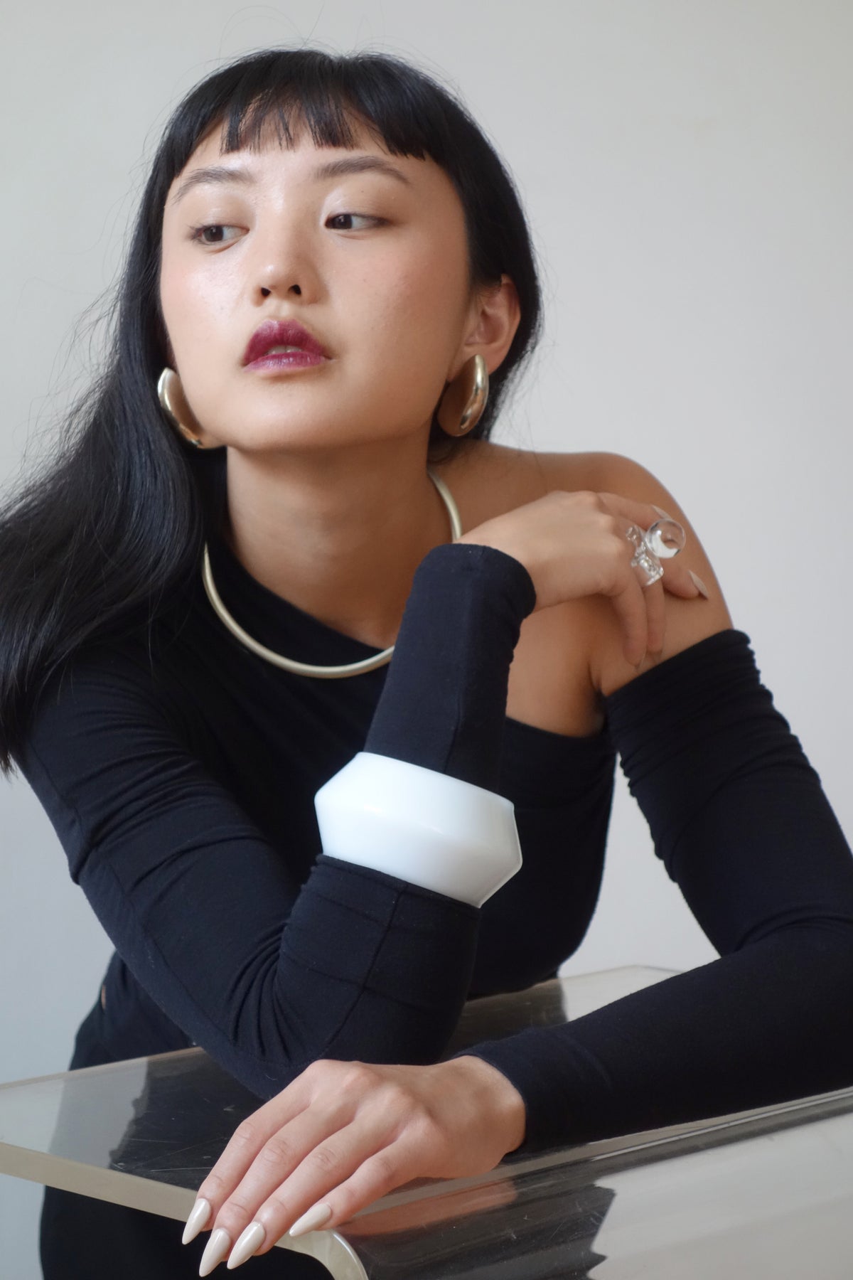 Woman wearing a black long-sleeve top with white bangle, leaning on a table.