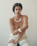 woman wearing a white arc-shaped porcelain necklace, white porcelain bangle, and pants with a plain background