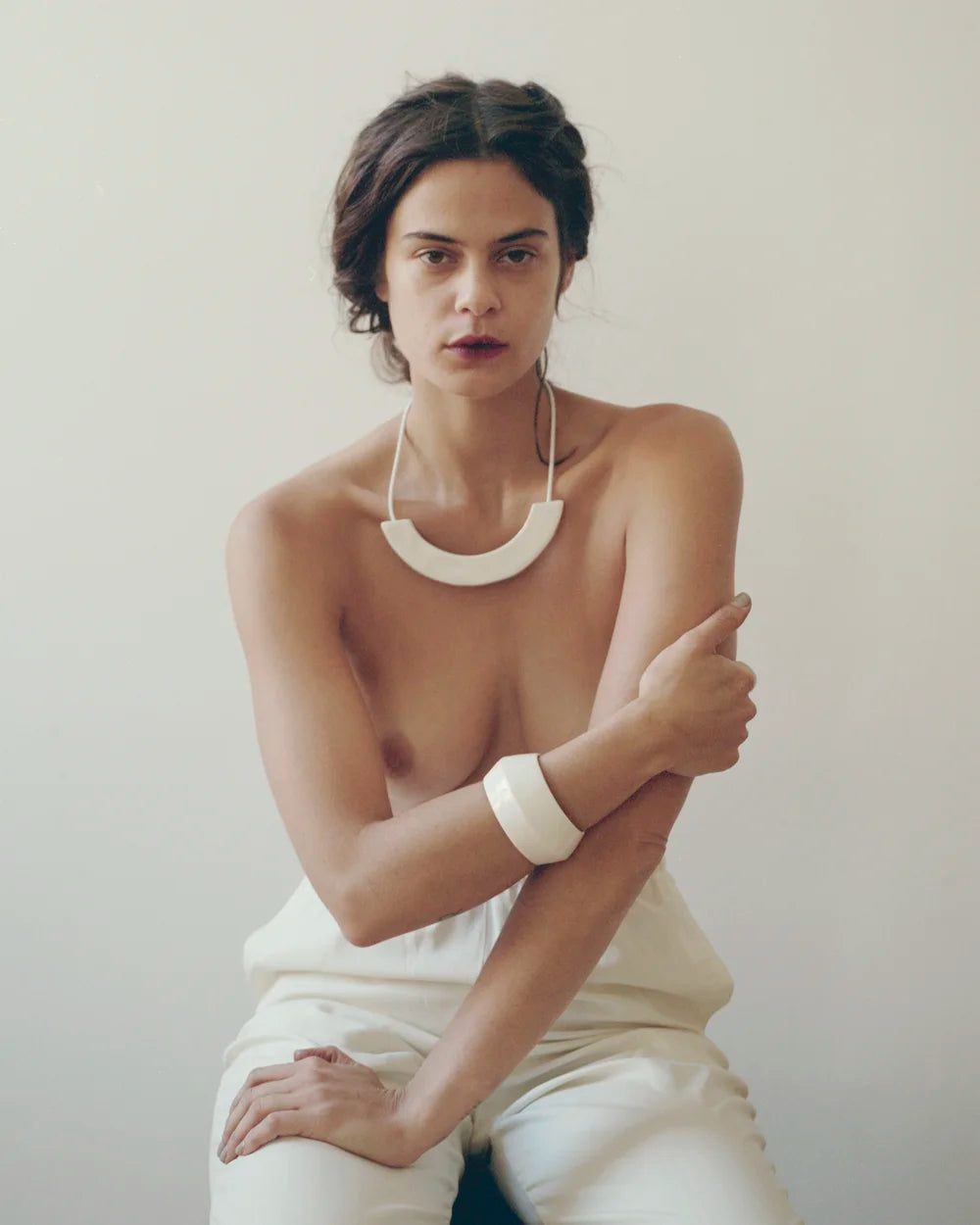 woman wearing a white arc-shaped porcelain necklace, white porcelain bangle, and pants with a plain background