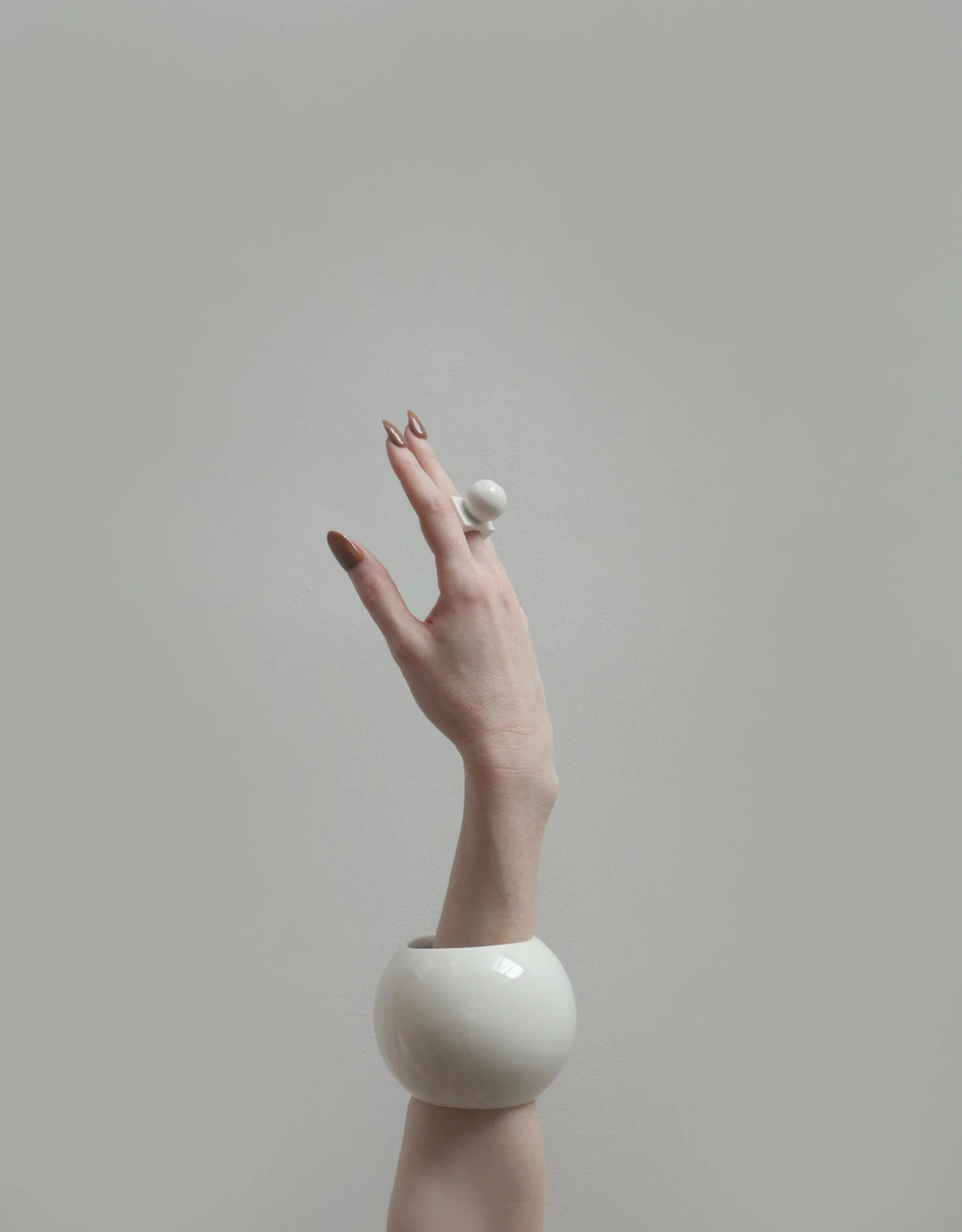 Hand wearing a white porcelain ring and bangle against a plain background