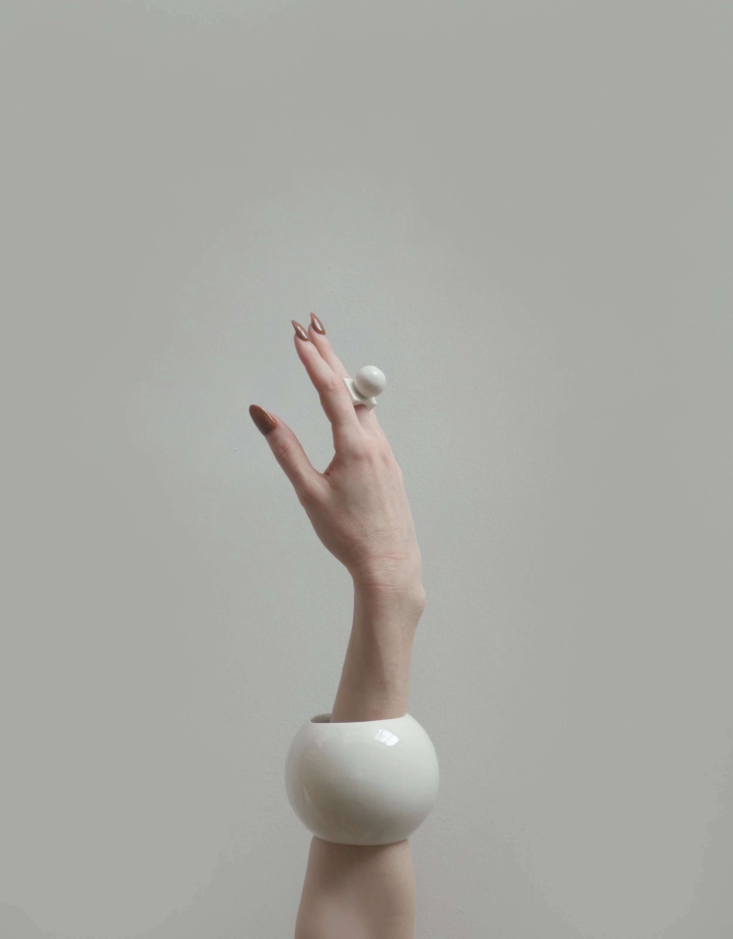 Hand wearing a white porcelain ring and bangle against a plain background