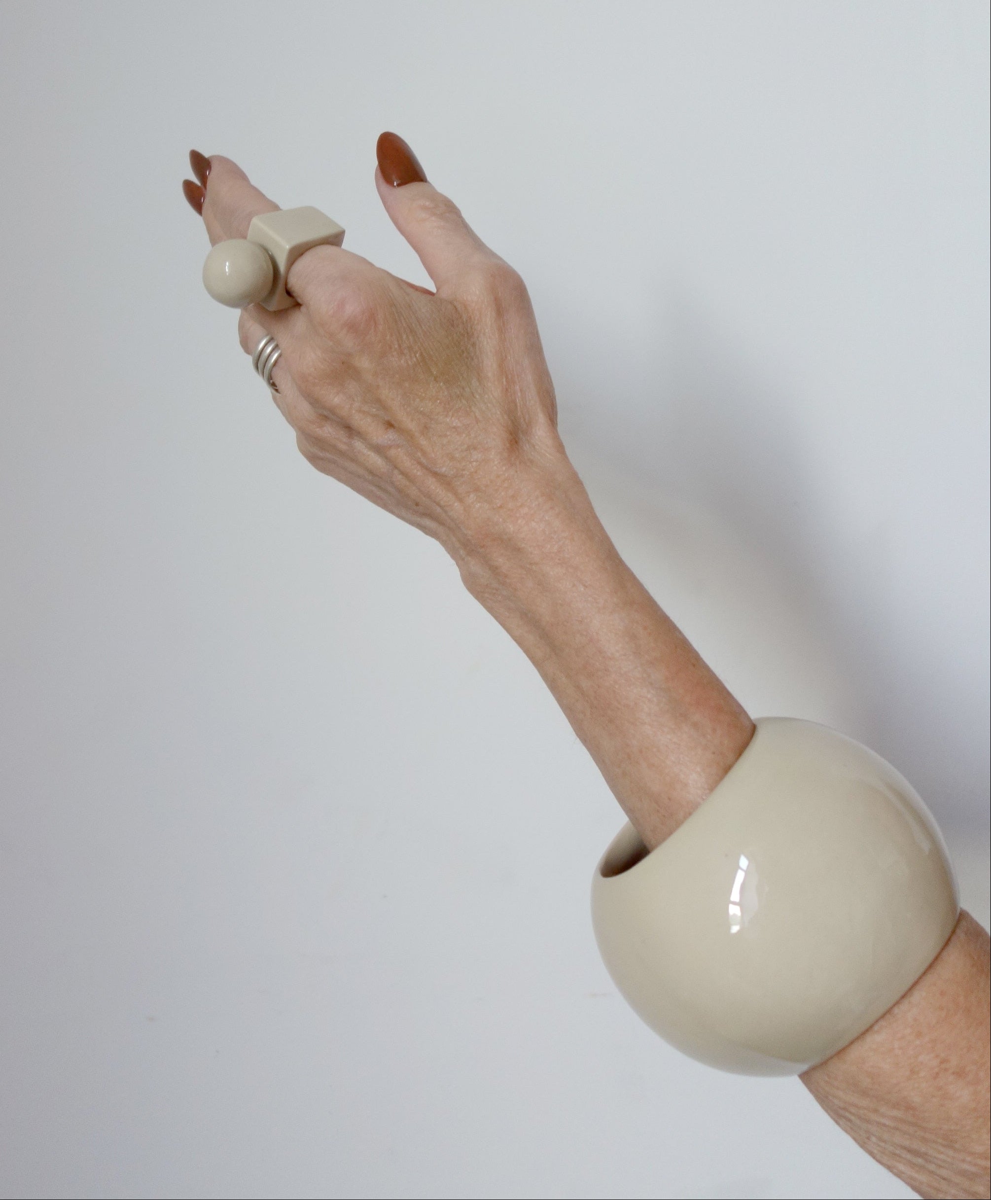 Hand wearing a large beige bracelet on a plain background