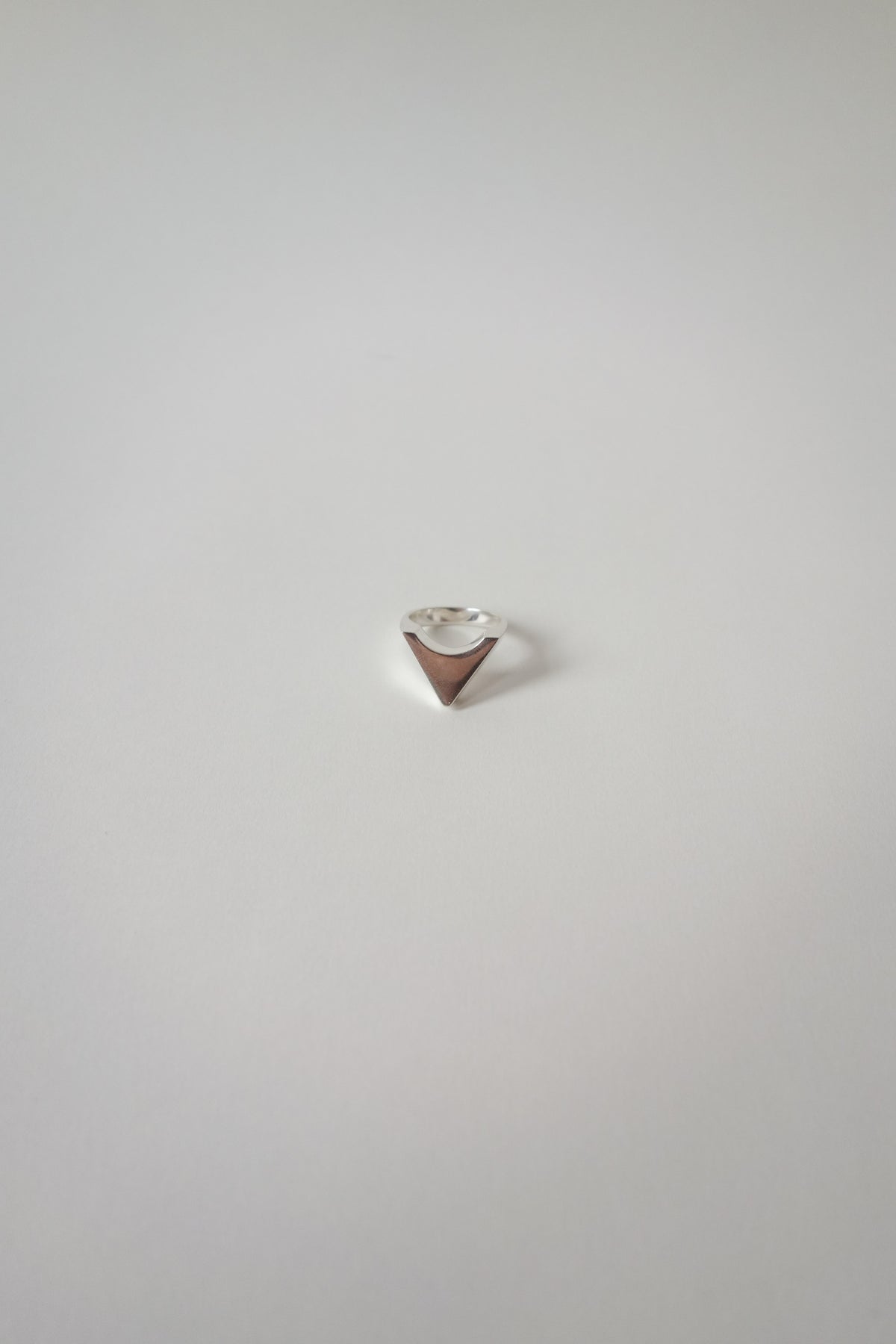 Small triangle-shaped silver ring on a light gray background