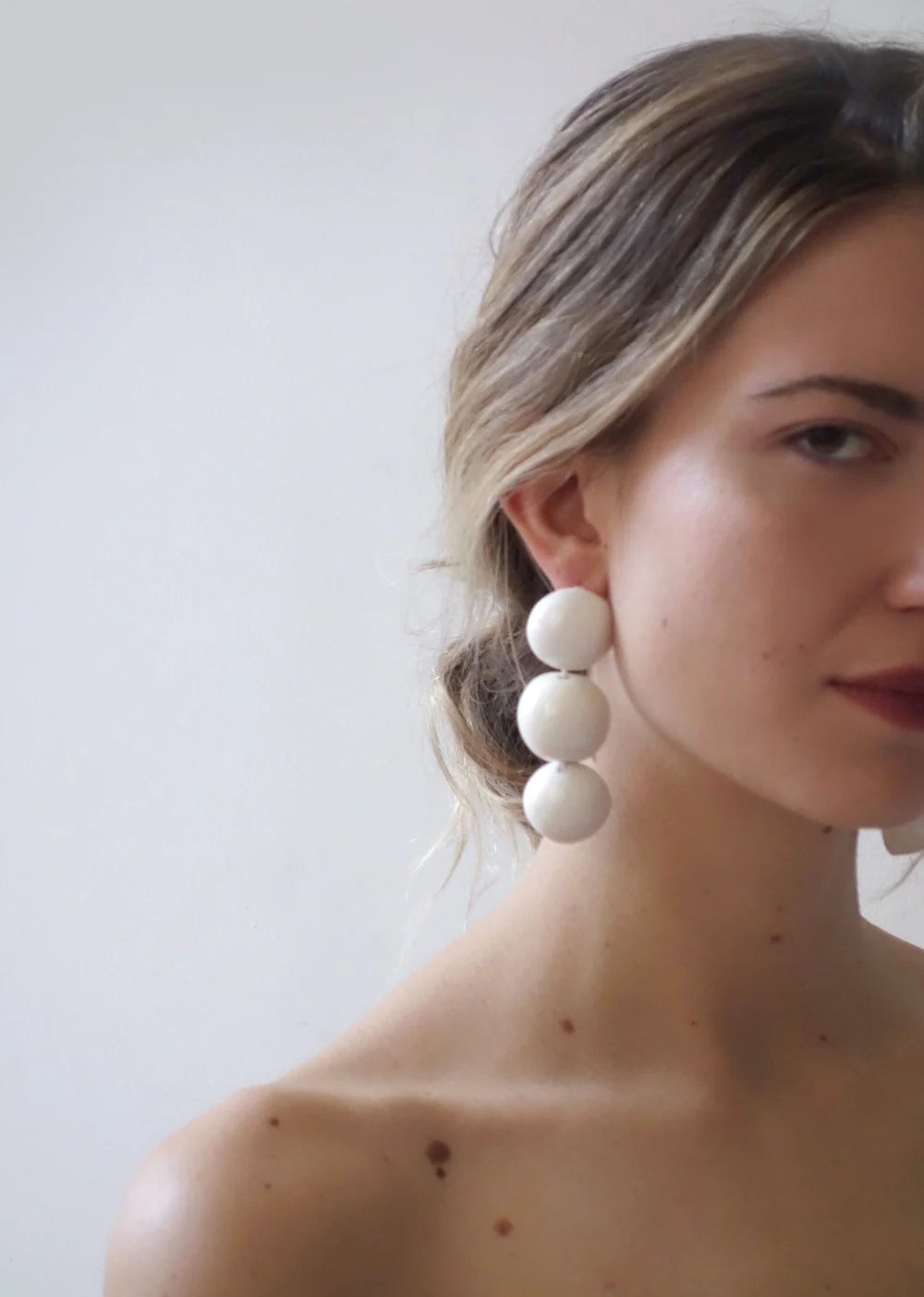 Woman wearing large white bead earrings against a plain background