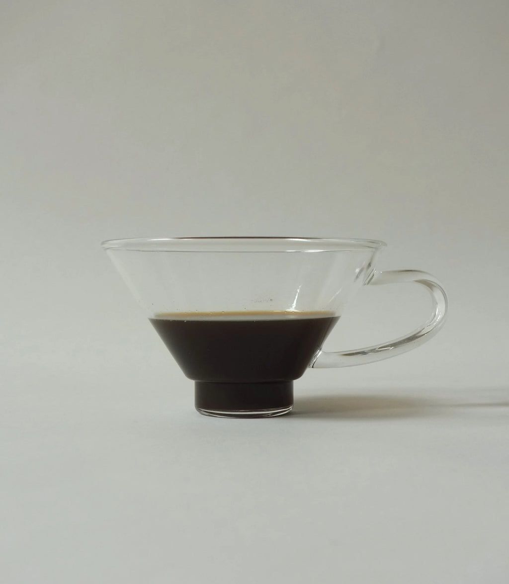Clear glass coffee cup with a handle filled with coffee on a white background