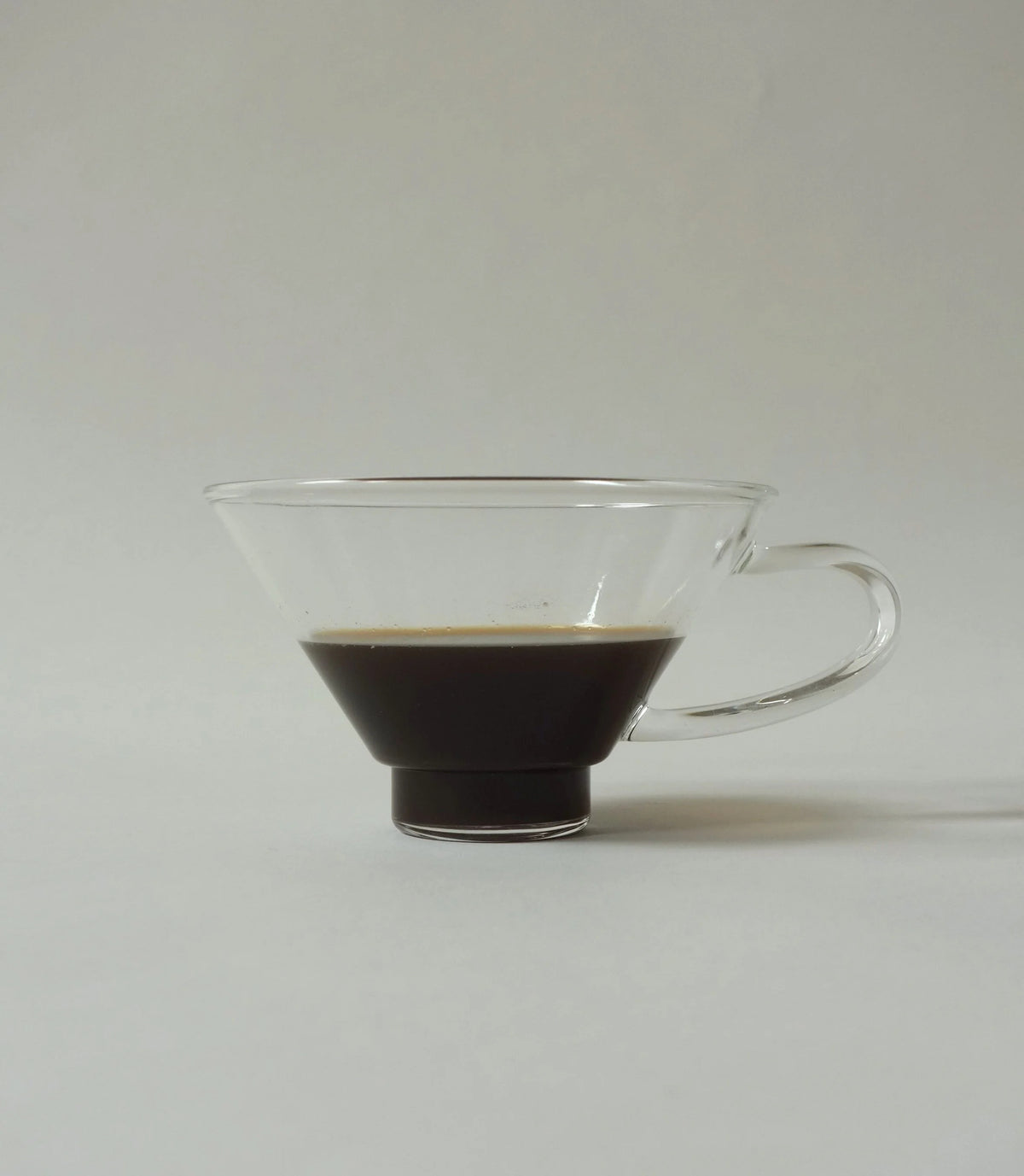 Clear glass coffee cup with a handle filled with coffee on a white background