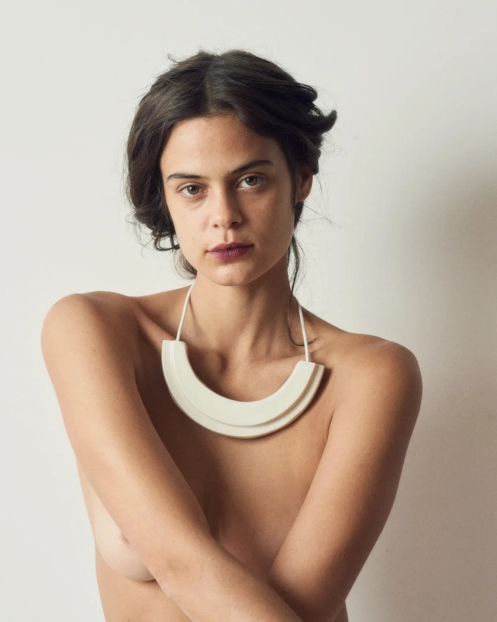 Woman wearing a white necklace against a plain background